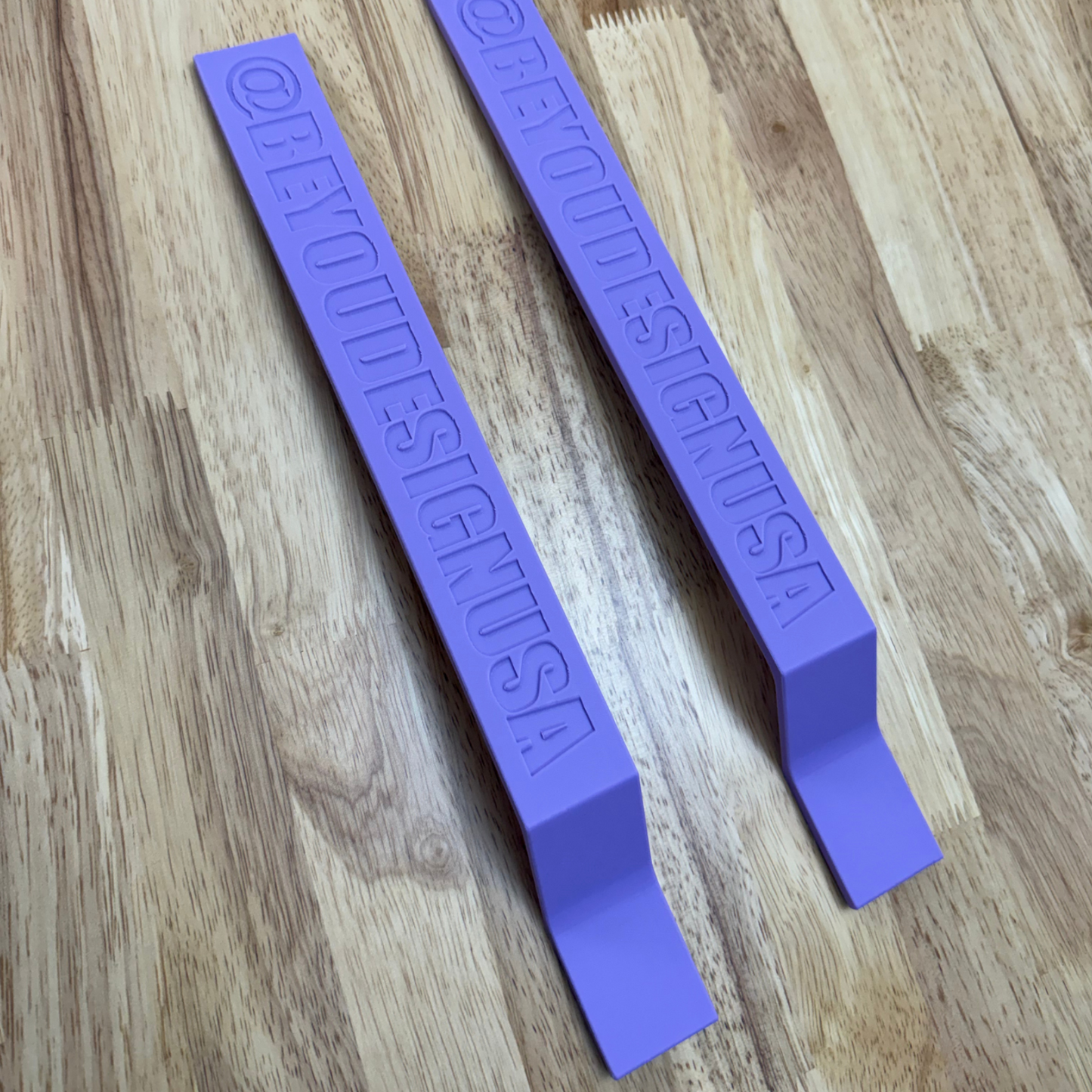 Two purple plastic tools with embossed text on a wooden surface
