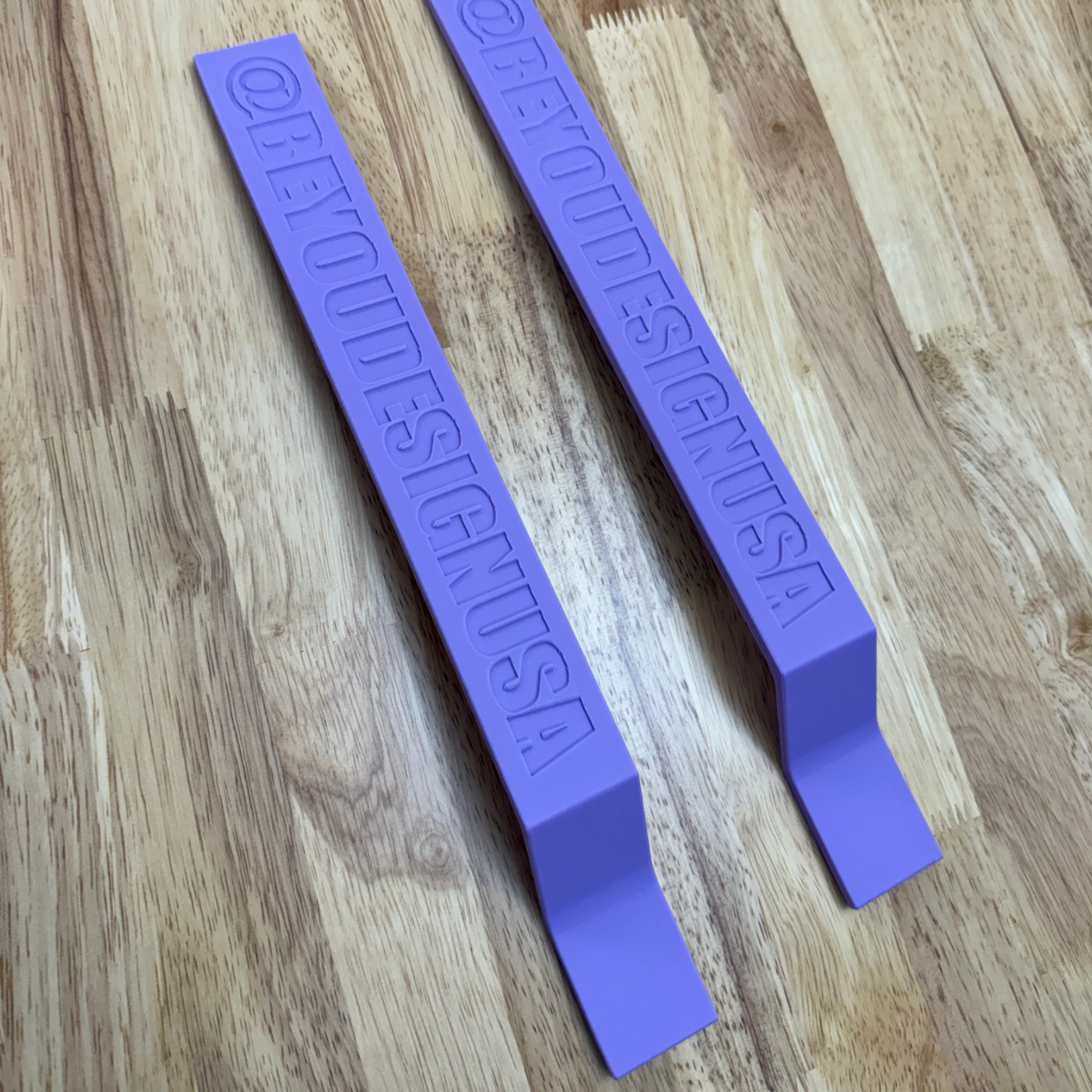 Two purple plastic tools with embossed text on a wooden surface